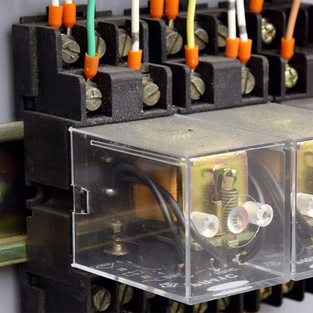 Na tym zdjęciu znajduje się zbliżenie na przekaźnik elektryczny z przezroczystą obudową, przez którą widać jego wewnętrzne elementy — cewki, styki i mechanizmy przełączające.