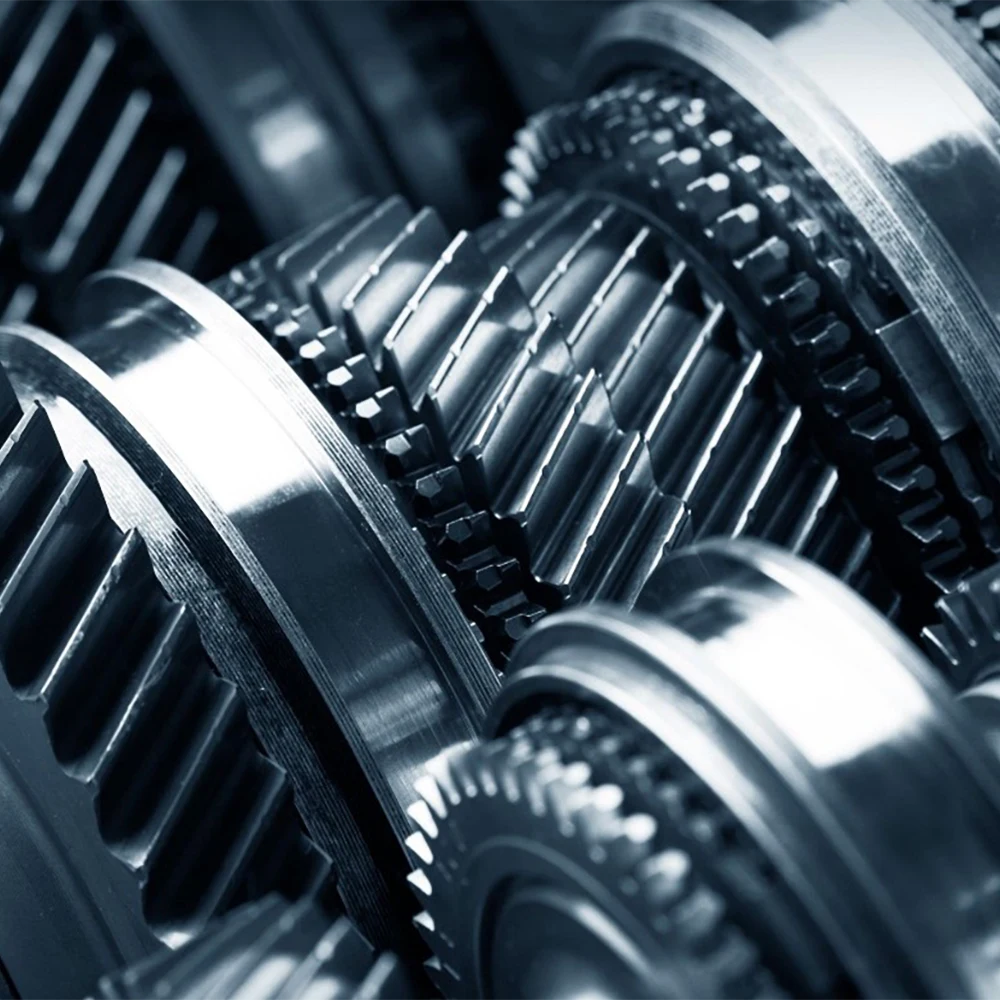 Na zdjęciu znajduje się zbliżenie na mechanizm zębaty – kilka metalowych kół zębatych osadzonych na wałkach.