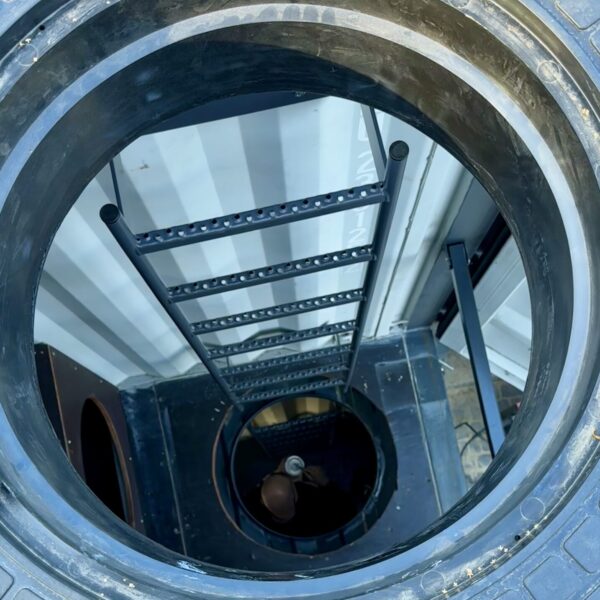 Na zdjęciu widoczny jest pionowy szyb techniczny z drabiną, najprawdopodobniej symulator wejścia do turbiny wiatrowej lub innego obiektu przemysłowego.